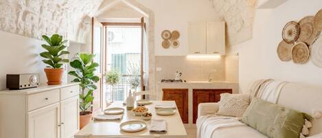 A cozy kitchen with a dining area, white cabinets, and a stone wall.