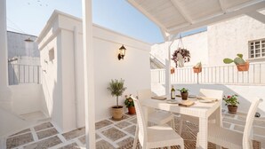 A covered outdoor seating area with a table and chairs, potted plants, and a hanging plant.