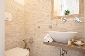 A bathroom with a stone wall, a large vessel sink, a towel rack, and toiletries. - Mia & Mimi – Accogliente Rifugio nel Centro Storico (Ostuni)