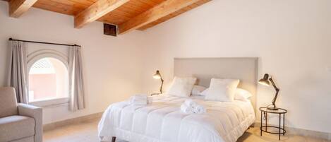 A bedroom with a large bed, two bedside lamps, a chair, and a window with curtains.