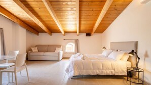 A bedroom with a bed, a sofa, a dining table with chairs, and a lamp. - Tower Palace 201 - Historic Modern Lofts (Bari)