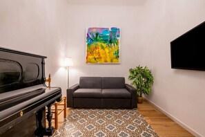 Un salon avec un piano, un canapé, un tapis à motifs, un tableau et un téléviseur.