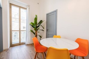 A dining area with a round table and four orange chairs, a potted plant, and a grey door.