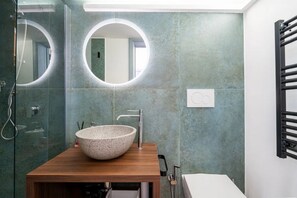 A modern bathroom with a wooden vanity, a large bowl sink, and two round mirrors.
