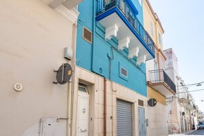 Un immeuble à plusieurs étages, doté d’une façade bleue et jaune, d’une porte blanche et d’un portail de garage fermé.