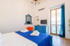 A hotel room with a bed, a blue dresser, a television, and a balcony with blue curtains.