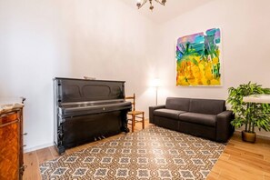 A living room with a piano, a sofa, a patterned rug, a painting, and a plant.