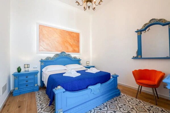 A bedroom with a blue bed, a blue dresser, a red chair, and a large painting on the wall.