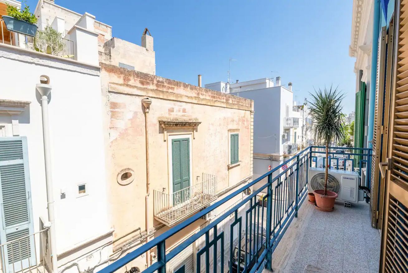Stretta via cittadina con edifici, un corrimano in metallo blu e un condizionatore Samsung sulla destra.