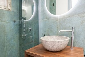 Une salle de bain dotée d’un lavabo sur pied, d’une douche moderne et d’un grand miroir.