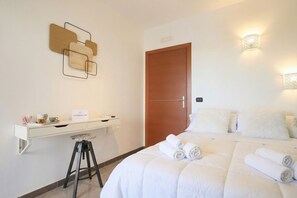 Ein Hotelzimmer mit Bett, Schreibtisch, Hocker, einer Tür und an der Wand befestigten Leuchten.