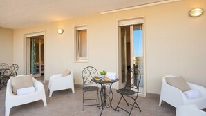 A balcony with white chairs, a table with a plant, and a sign.