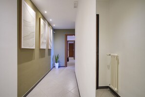 Un couloir avec un radiateur, une plante en pot et des œuvres d’art encadrées accrochées au mur.