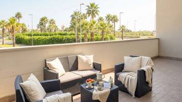 A balcony with wicker furniture, a coffee table with a fruit bowl, and a view of palm trees and greenery.