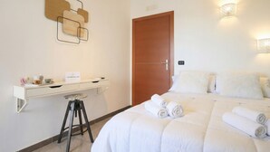 A hotel room with a bed, a desk, a stool, a door, and wall-mounted light fixtures.