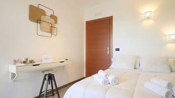 Ein Hotelzimmer mit Bett, Schreibtisch, Hocker, einer Tür und an der Wand befestigten Leuchten.
