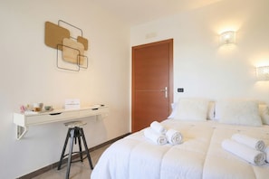 A hotel room with a bed, a desk, a stool, a door, and wall-mounted light fixtures.