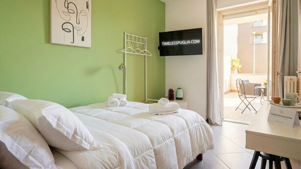 A hotel room with a bed, a TV, a desk, and a view of the outside.