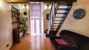 A cozy living room with a wooden floor, a black leather sofa, a staircase, and a bookshelf with decorative items. - Sofia - Classical Residence (Bari)