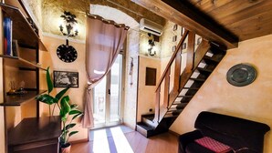 A cozy living room with a staircase, wooden beams, a black sofa, a potted plant, and a wall clock. - Sofia - Classical Residence (Bari)