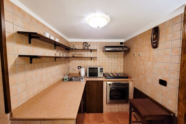 A compact kitchen with a microwave, toaster, and oven. There are shelves above the counter and a clock on the wall.