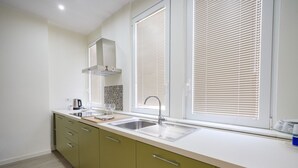 A modern kitchen with a double sink, green cabinets, and a window with blinds. - Calle Suite - Modern Apartment with Balcony (Bari)