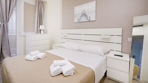A hotel room with a bed, a nightstand, a lamp, a painting on the wall, and a window with curtains. - Calle Suite - Modern Apartment with Balcony (Bari)
