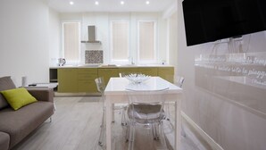 A modern kitchen with a dining area, a sofa, and a TV mounted on the wall. - Calle Suite - Modern Apartment with Balcony (Bari)