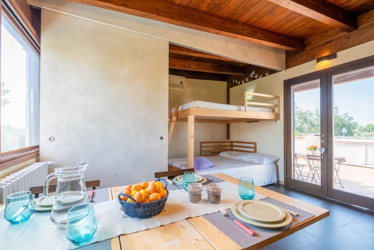 Una stanza accogliente con un letto a castello, un tavolo da pranzo apparecchiato con piatti, bicchieri e un cesto di arance.