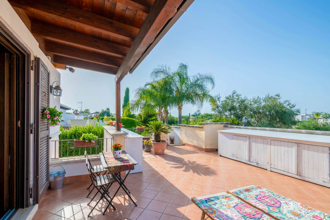 Una terrazza sul tetto con una pergola in legno, un tavolo con sedie, piante in vaso e vista sul verde circostante e sugli edifici.