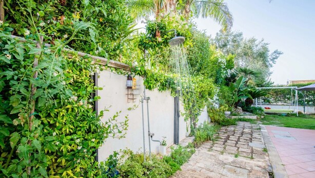 Ein Gartenweg führt zu einem weißen Gebäude mit Wasserspiel und Metallrohr.
