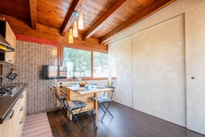 A compact kitchen with a wooden ceiling, a dining area with a table and chairs, and a large window providing natural light. - Villa Eden - Wellness Oasis (Bisceglie)