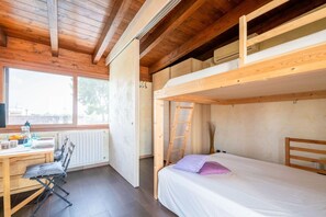 A compact room with a bunk bed, a desk with a chair, and a window providing natural light.