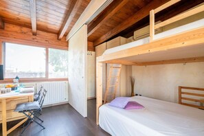Une pièce de taille modeste, équipée d’un lit superposé, d’un bureau avec une chaise et d’une fenêtre laissant entrer la lumière naturelle.