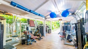 Ein überdachter Fitnessraum mit Trainingsgeräten, Laufband und Ergometer.
