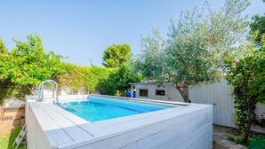 Ein rechteckiger Swimmingpool mit Holzterrasse, umgeben von üppiger Vegetation und einem weißen Zaun.