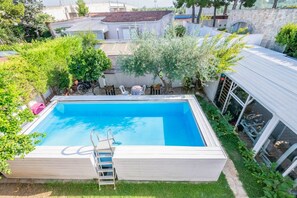 Une piscine rectangulaire avec un escalier, entourée de verdure et délimitée par une clôture blanche.