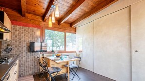 Eine kompakte K üche mit Holzbalkendecke, ein Essbereich mit Tisch und Stühlen sowie ein großes Fenster für natürliches Licht.