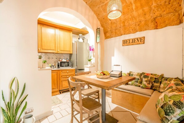 A cozy kitchen with wooden cabinets, a dining table, and a sofa with a 'BELIEVE' sign.