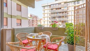 A balcony with wicker chairs and a table set for dining, surrounded by potted plants and overlooking a residential building. - Moonlight - Jacuzzi Suite (Bari)