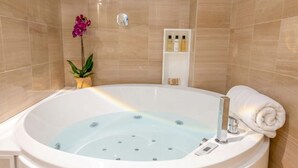 A bathroom with a large bathtub, a potted orchid, and a shelf with toiletries. - Moonlight - Jacuzzi Suite (Bari)
