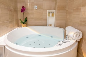 A bathroom with a large bathtub, a potted orchid, and a shelf with toiletries.
