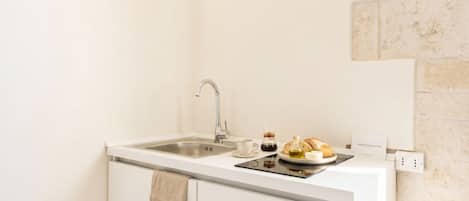 A small kitchenette with a sink, a coffee maker, a bottle of olive oil, and a plate of bread.