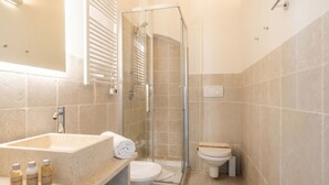 A bathroom with a glass-enclosed shower, a sink with toiletries, and a toilet.
