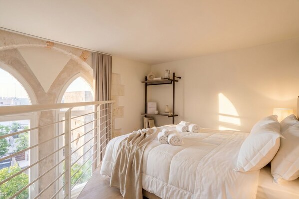 Une chambre à coucher avec un lit, une table de chevet, une étagère et une vue sur l’extérieur par une fenêtre en arc de cercle.