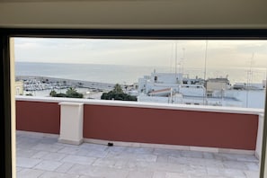 A balcony with a view of the sea and a parking area.