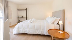 A neatly arranged hotel room with a bed, a bedside table with a lamp, a wooden floor, and a window with curtains.