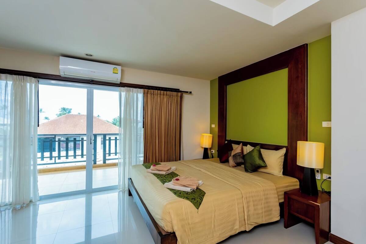 A hotel room with a bed, two bedside lamps, a window with curtains, and an air conditioning unit.