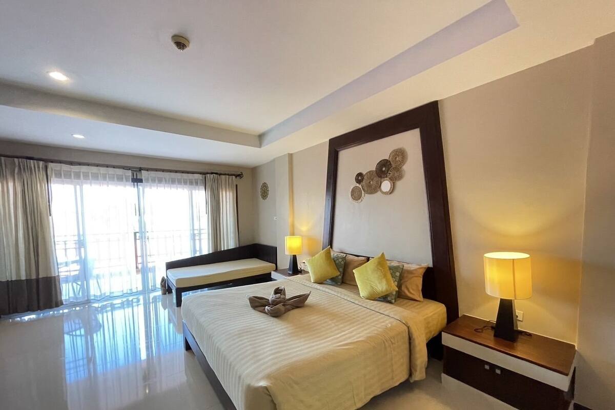 A hotel room with a large bed, a smaller bed, a desk with a lamp, and a large window with curtains.