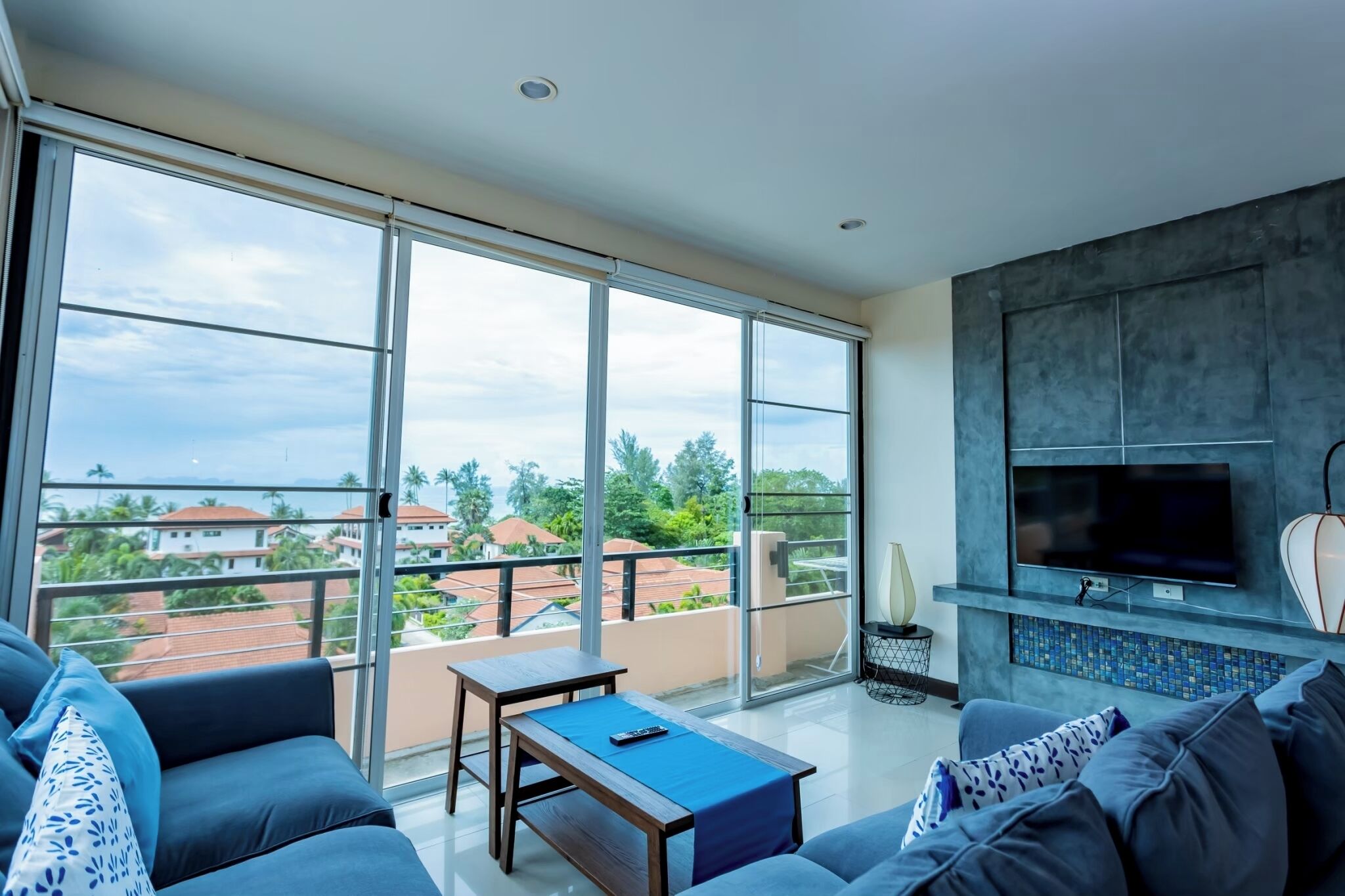 A modern living room with a large balcony, a flat-screen TV, and a view of the neighborhood.